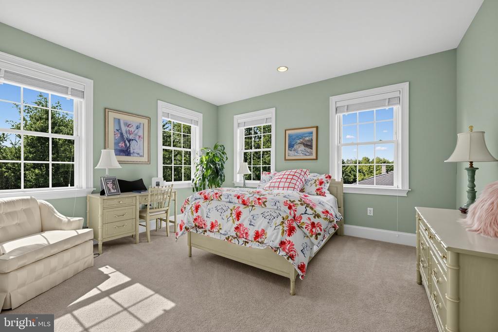Bedroom with floral bedding, sage green walls, large windows, and a cream loveseat.