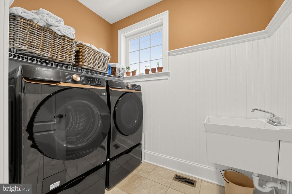 Laundry room with dark front-loading washer and dryer, wicker baskets, and a utility sink.