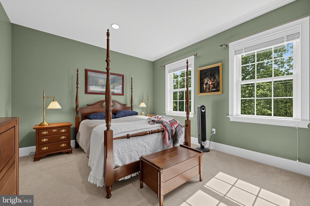 Bedroom with a dark wood four-poster bed, sage-green walls, and windows overlooking leafy trees.