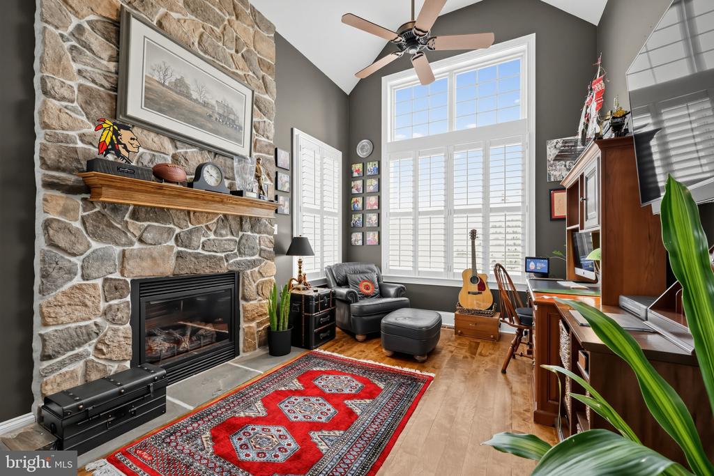 Living room with a stone fireplace, vaulted ceiling, tall windows, leather seating, and a red patterned rug.