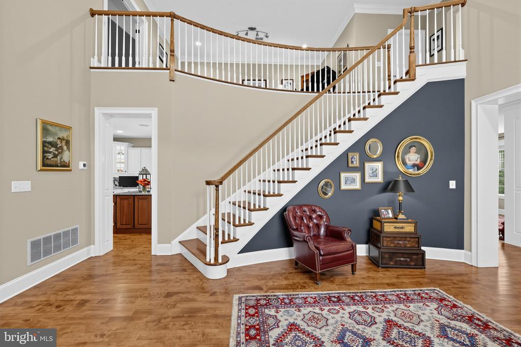 Foyer with a sweeping staircase, dark blue accent wall, leather chair, and patterned rug.