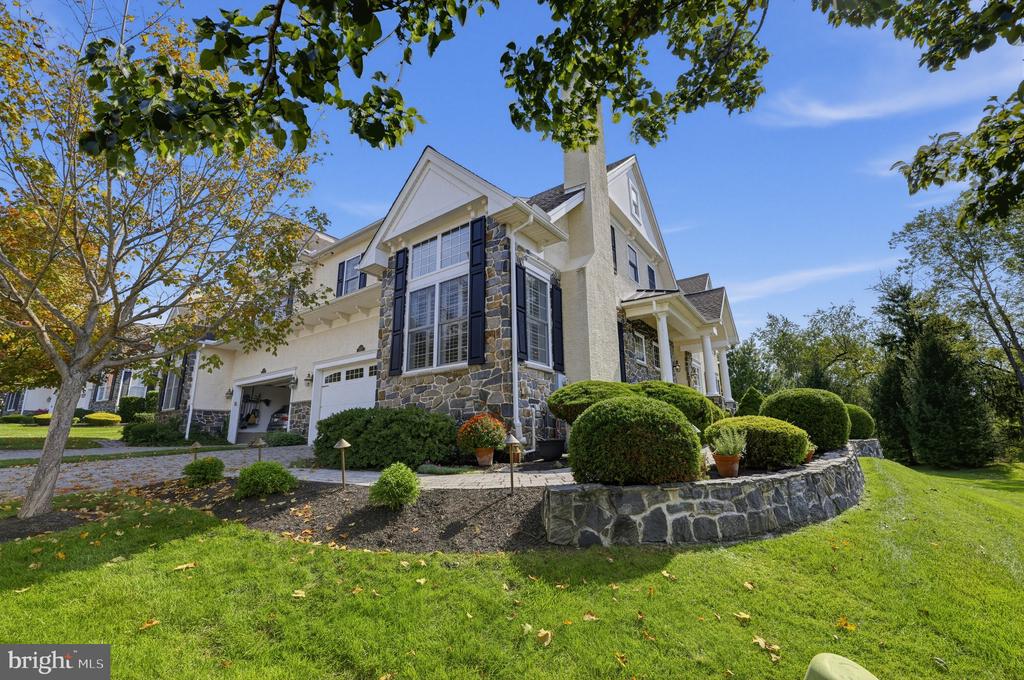 Two-story home with stone accents and black shutters, framed by rounded shrubs and a raised stone planter.