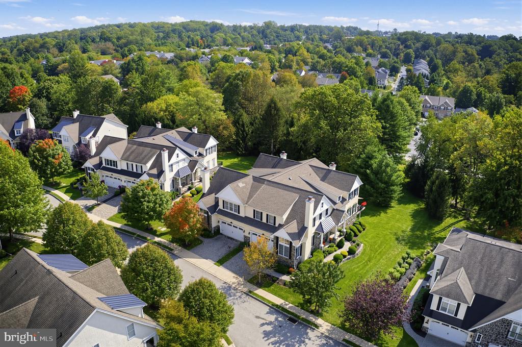 Aerial view of a large gray-roofed home among leafy suburban homes and wooded hills.