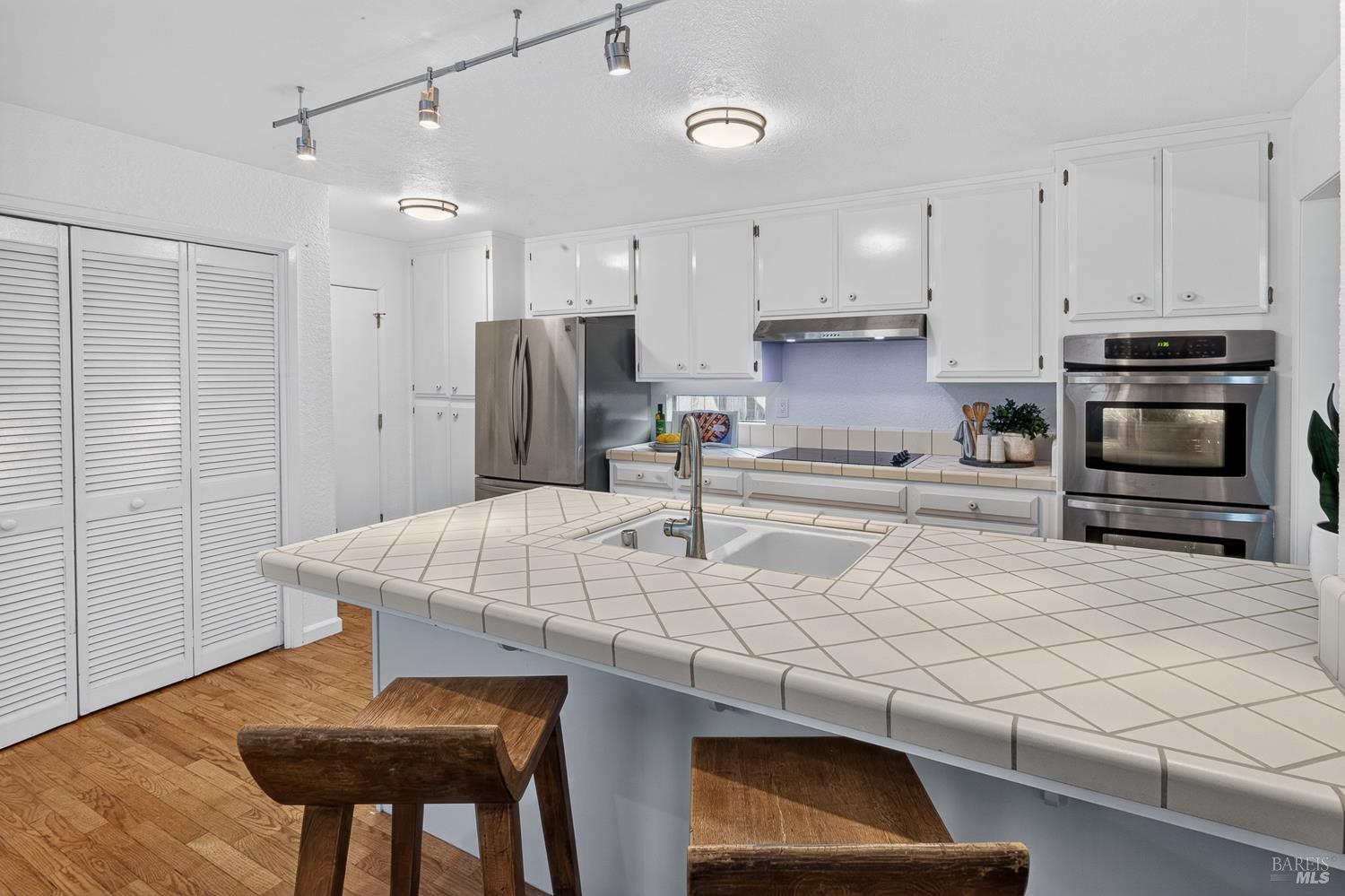 Kitchen with a large tiled island, white cabinetry, stainless steel appliances, and hardwood floors.