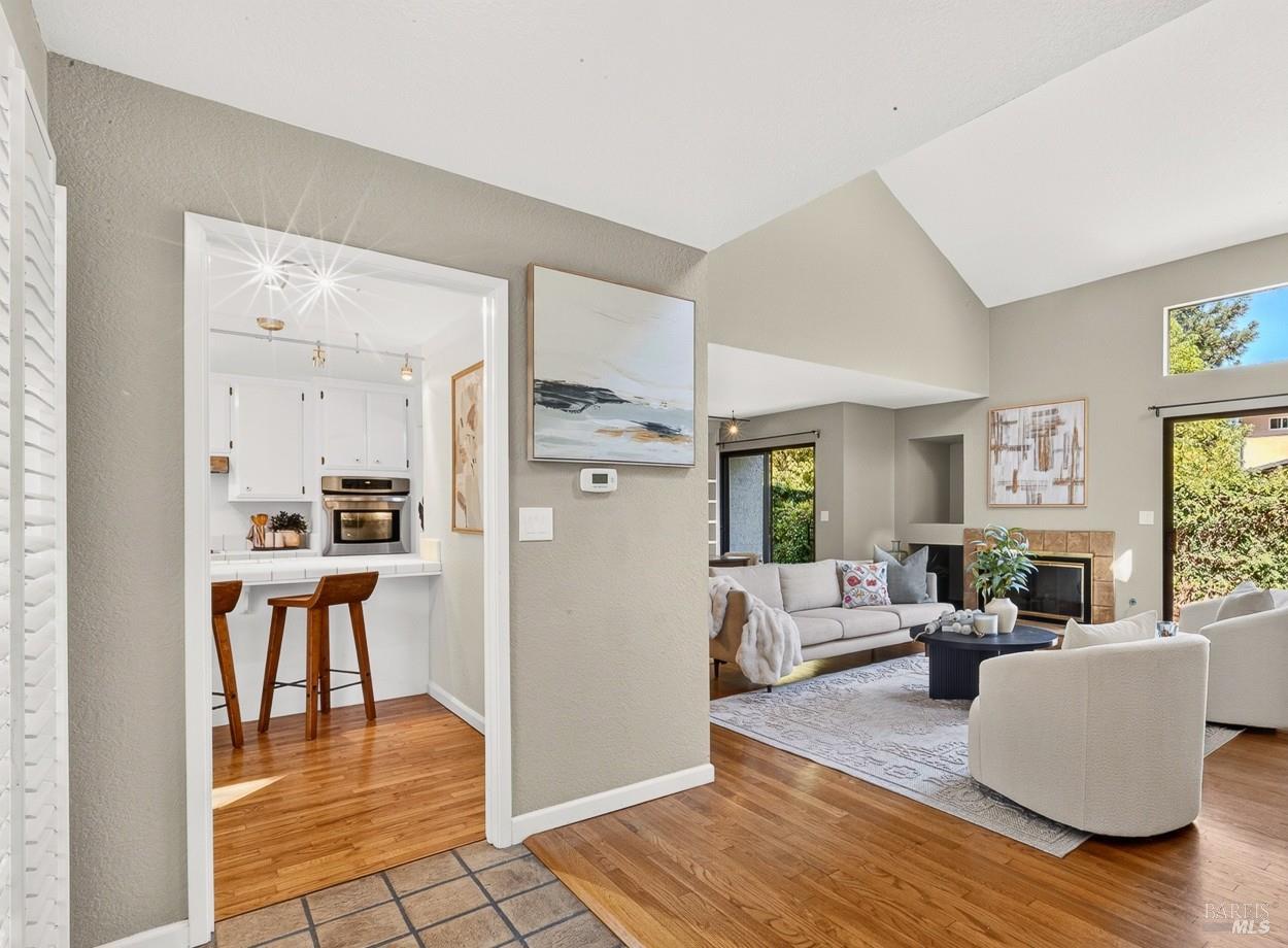 Living room with vaulted ceiling and fireplace, adjoining a white kitchen with a breakfast bar.