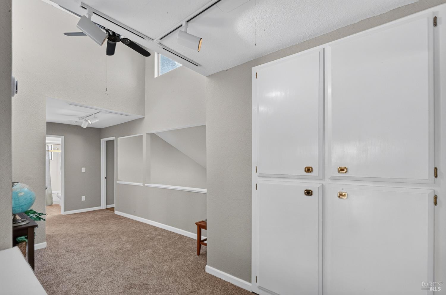 Carpeted room with large built-in white cabinets and a ceiling fan beside an open under-stair area.