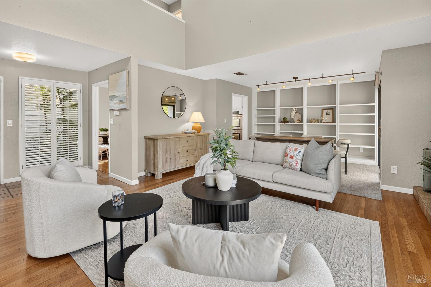 Staged living room with gray seating, hardwood floors, and built-in white shelving.