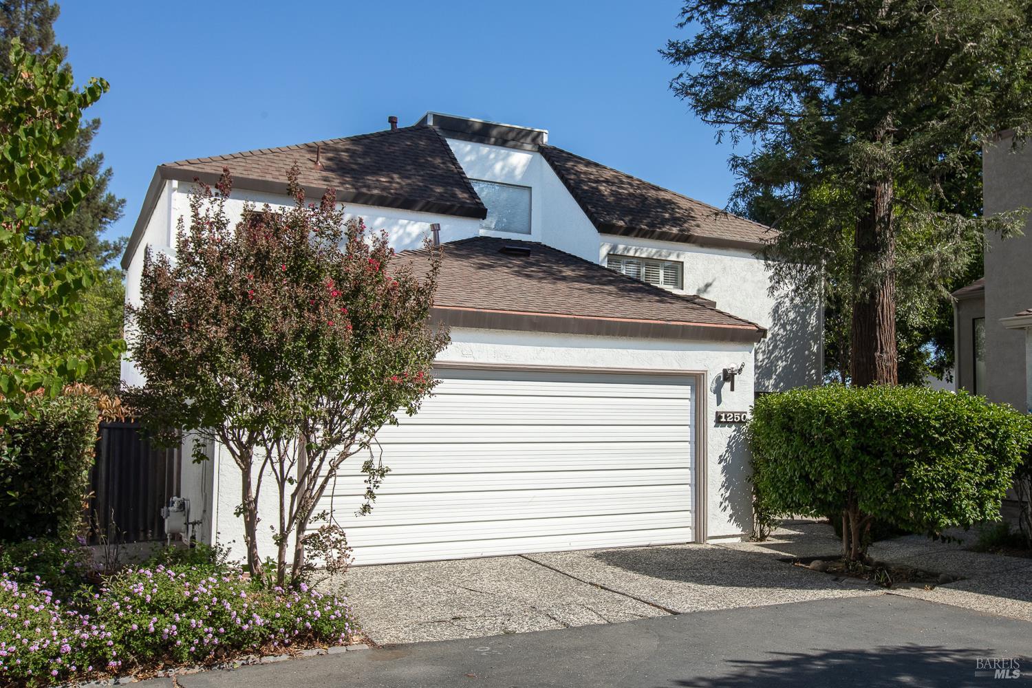 Two-story white stucco home with a brown shingle roof, double garage, and landscaped front yard.