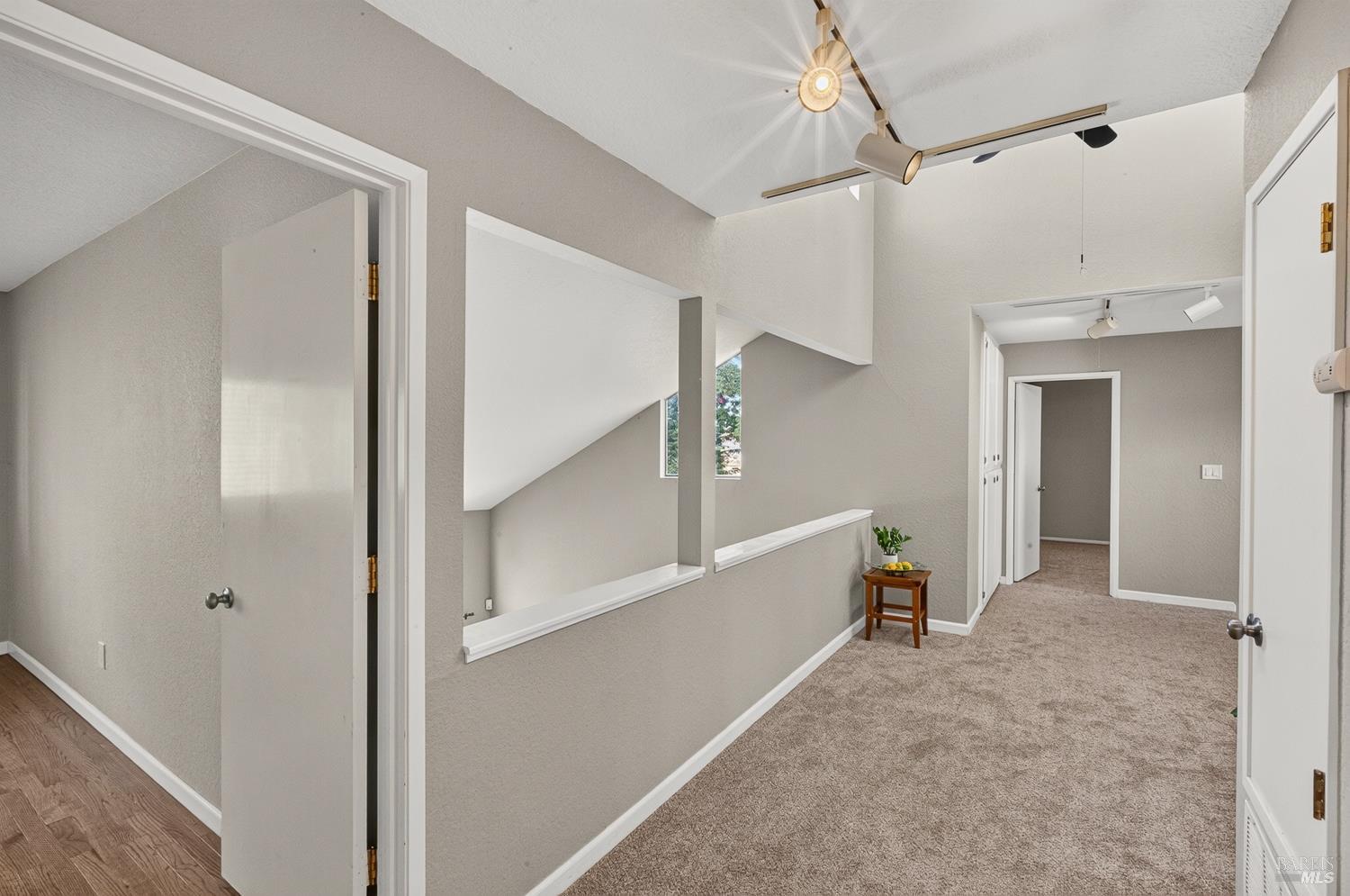 Carpeted upstairs hallway with a vaulted ceiling, track lighting, and an open loft overlook.