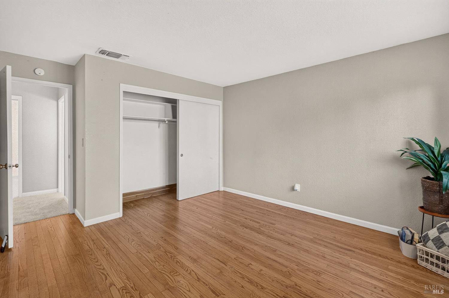 Vacant bedroom with hardwood floors and a partially open sliding-door closet.