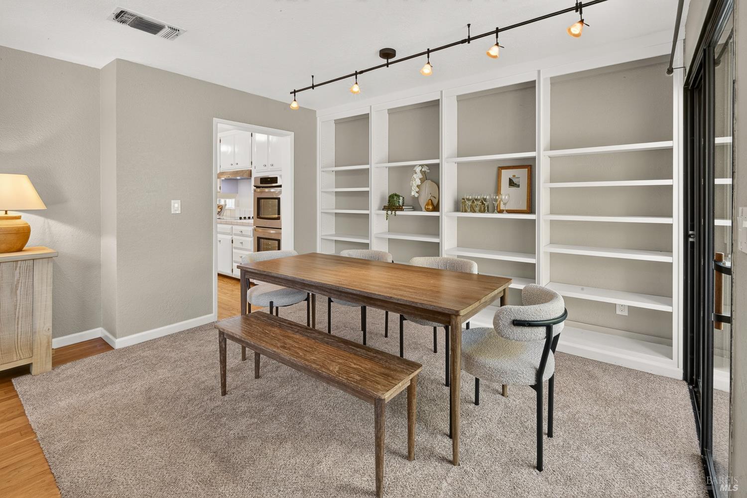 Dining room with built-in shelves, a wooden table and bench, and a doorway to the kitchen.