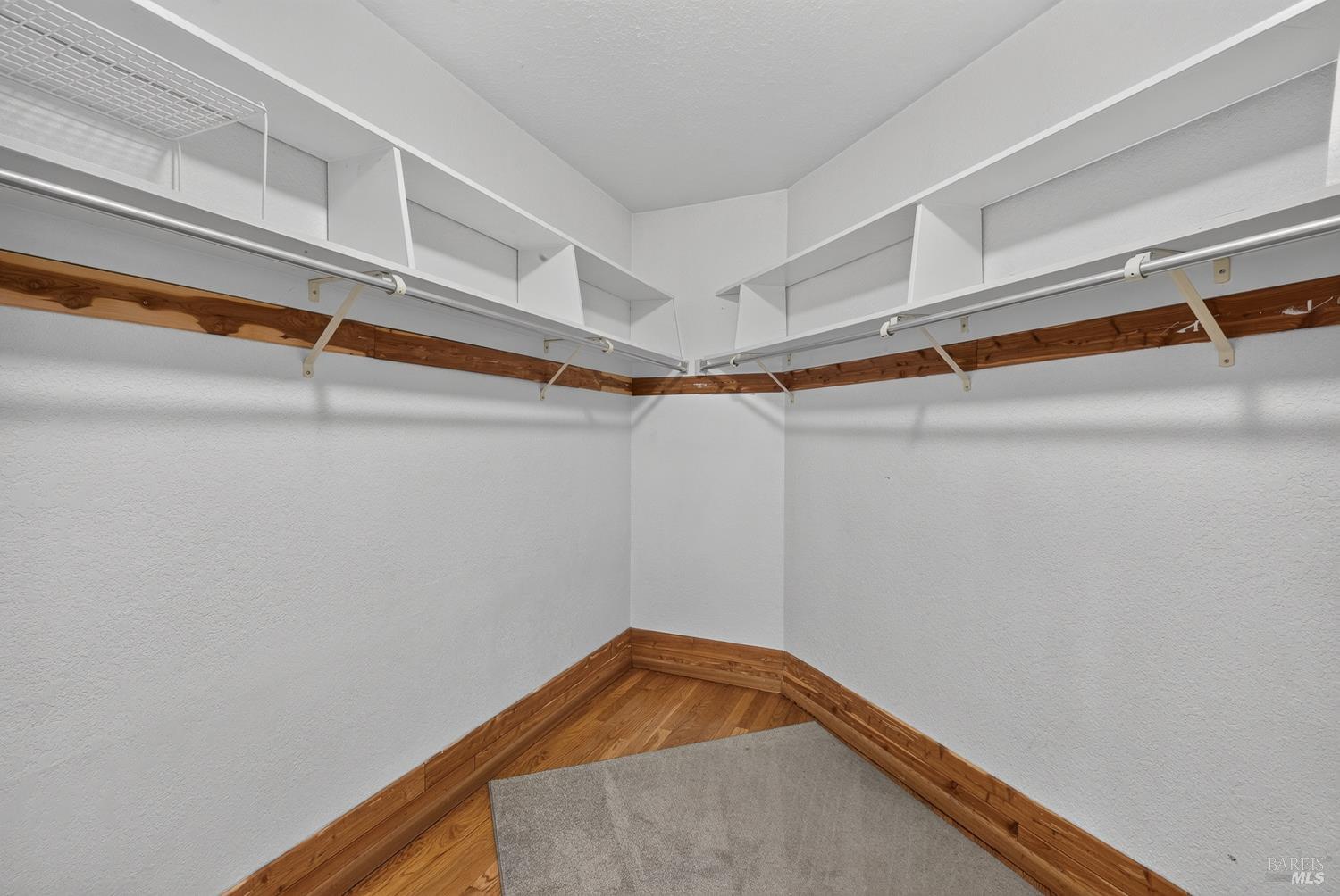 Walk-in closet with wraparound shelves and hanging rods, wood trim, and a gray carpet runner.