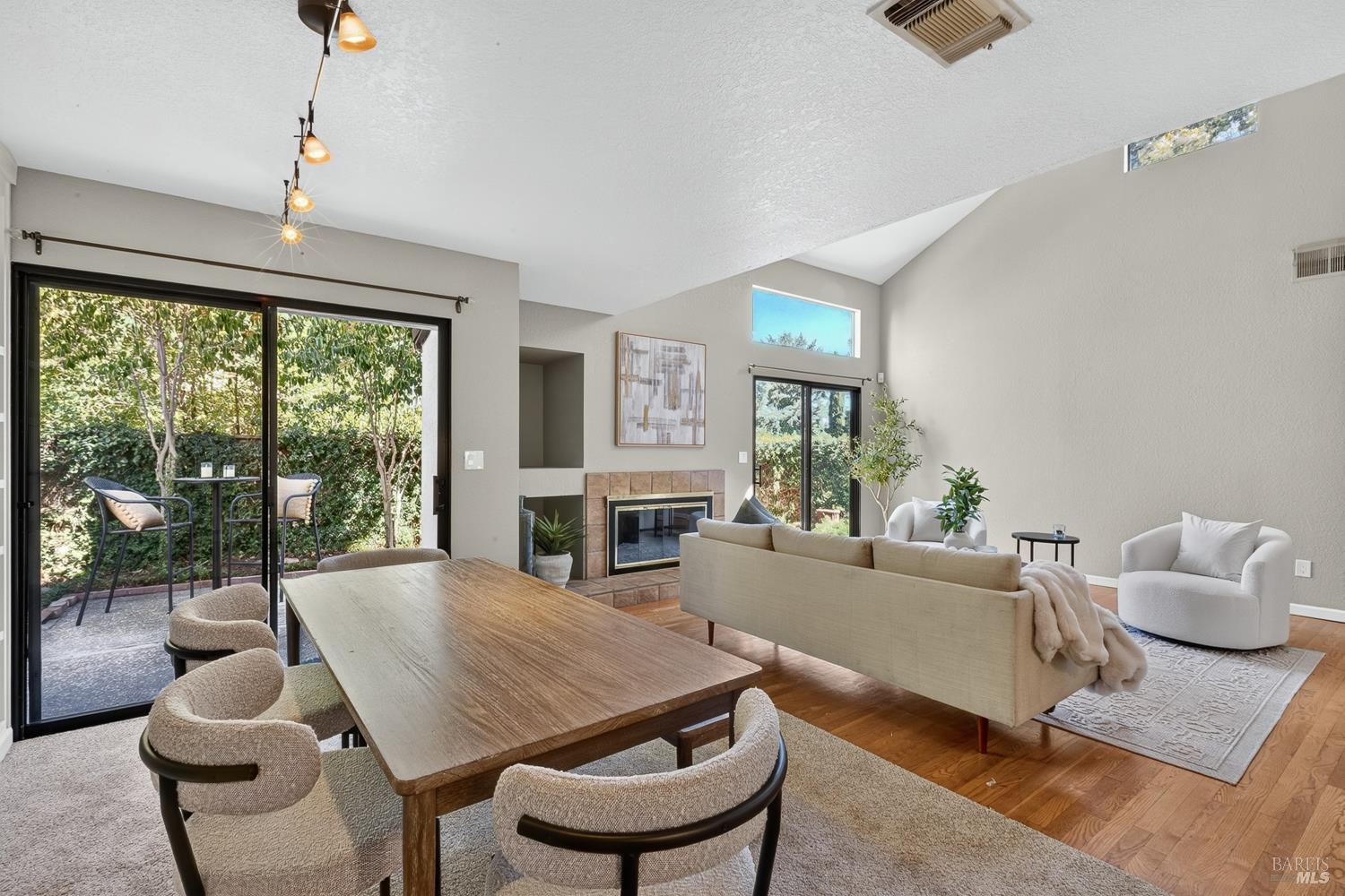 Living and dining room with a tiled fireplace, vaulted ceiling, and sliding doors to a leafy garden.