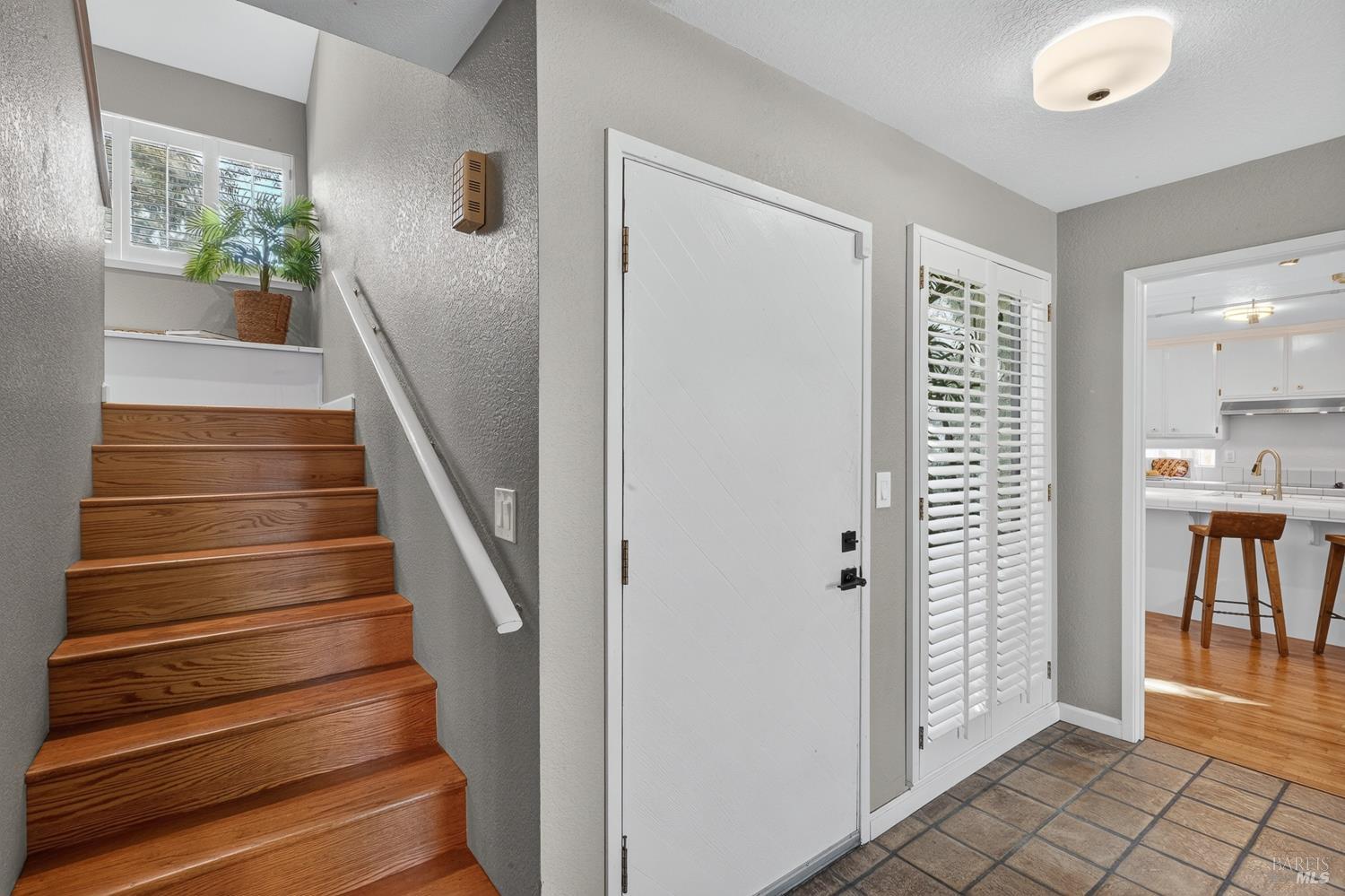 Entryway with a white front door, tiled floor, and wooden stairs leading up beside a shuttered window.