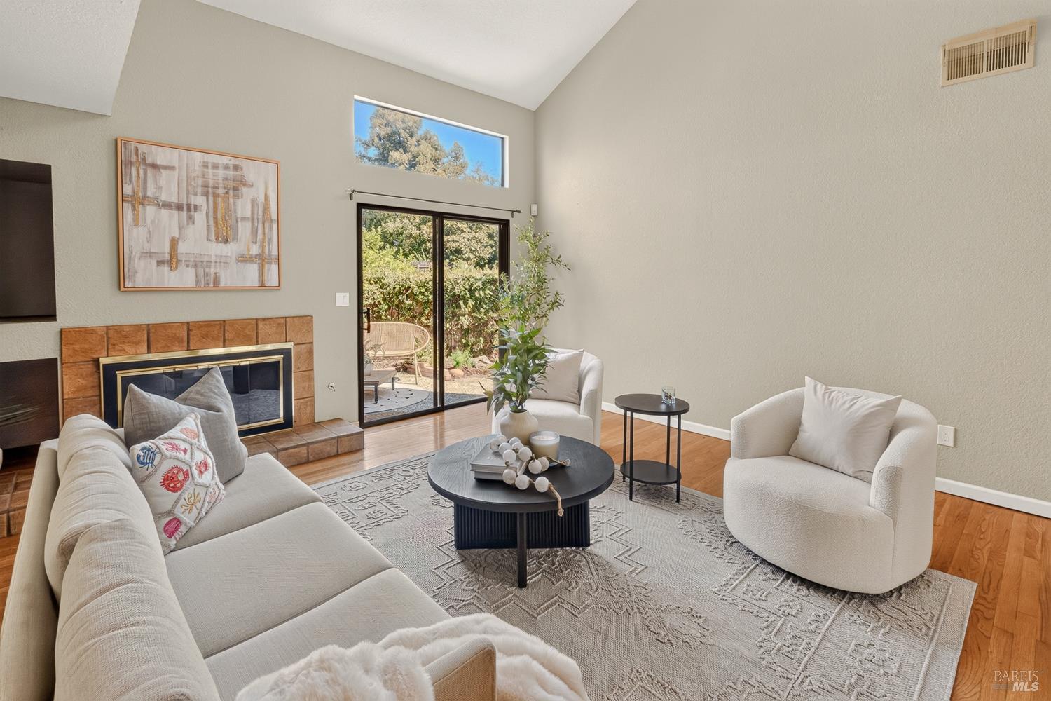 Staged living room with a tiled fireplace, vaulted ceiling, and sliding glass doors to a garden patio.