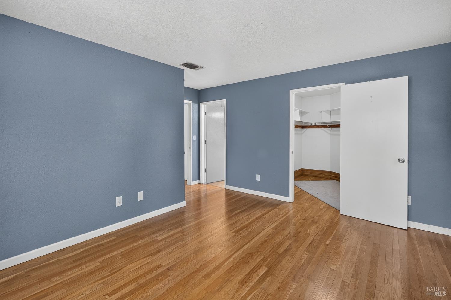 Vacant bedroom with blue walls, hardwood floors, and an open walk-in closet.
