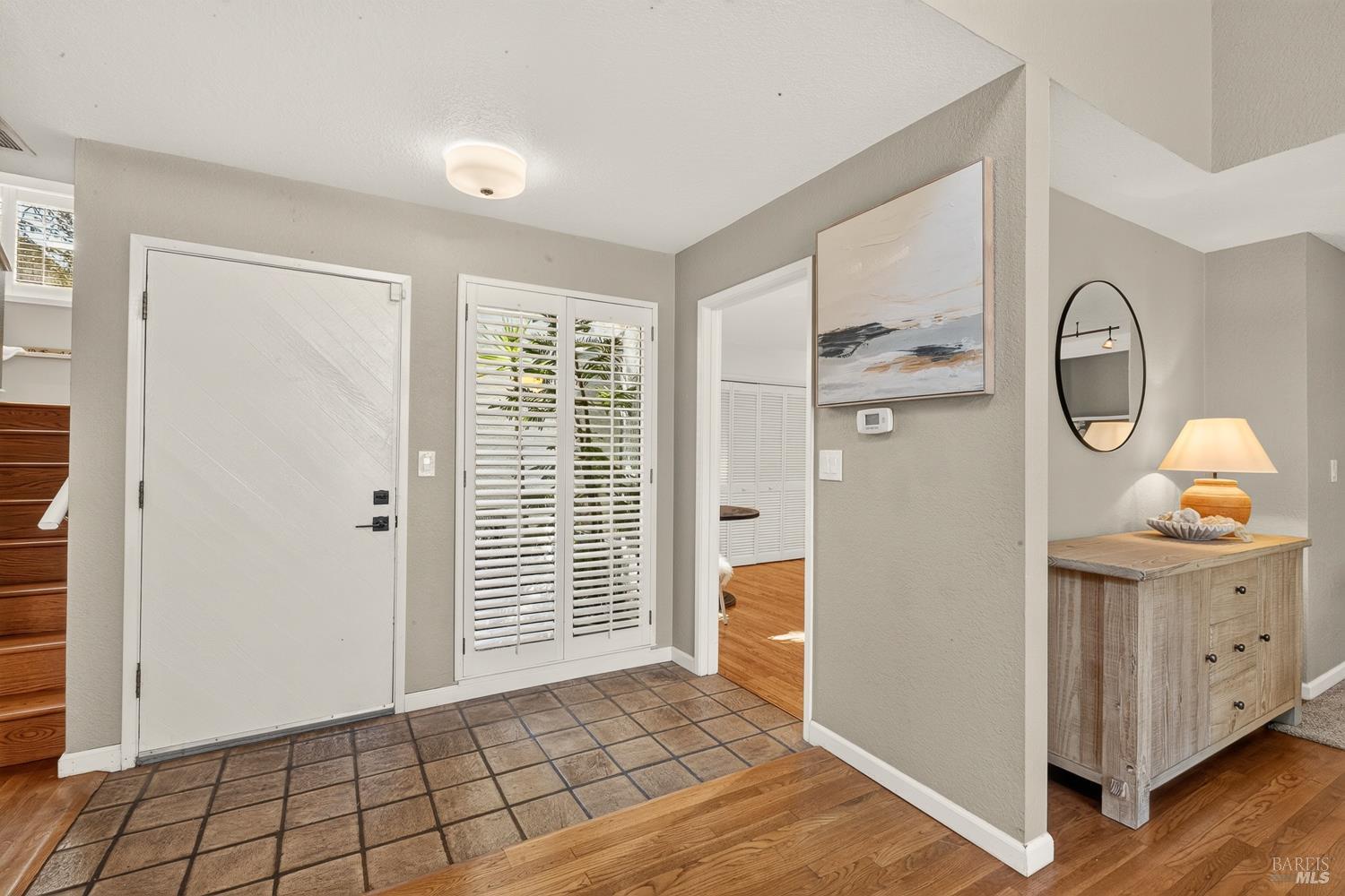 Entry foyer with tiled flooring, a white front door, shuttered glass doors, and a console table.