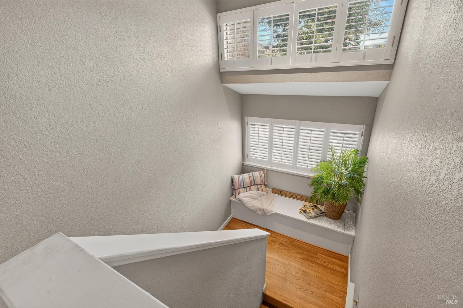 Staircase landing with a window seat, potted palm, hardwood floors, and plantation shutters.