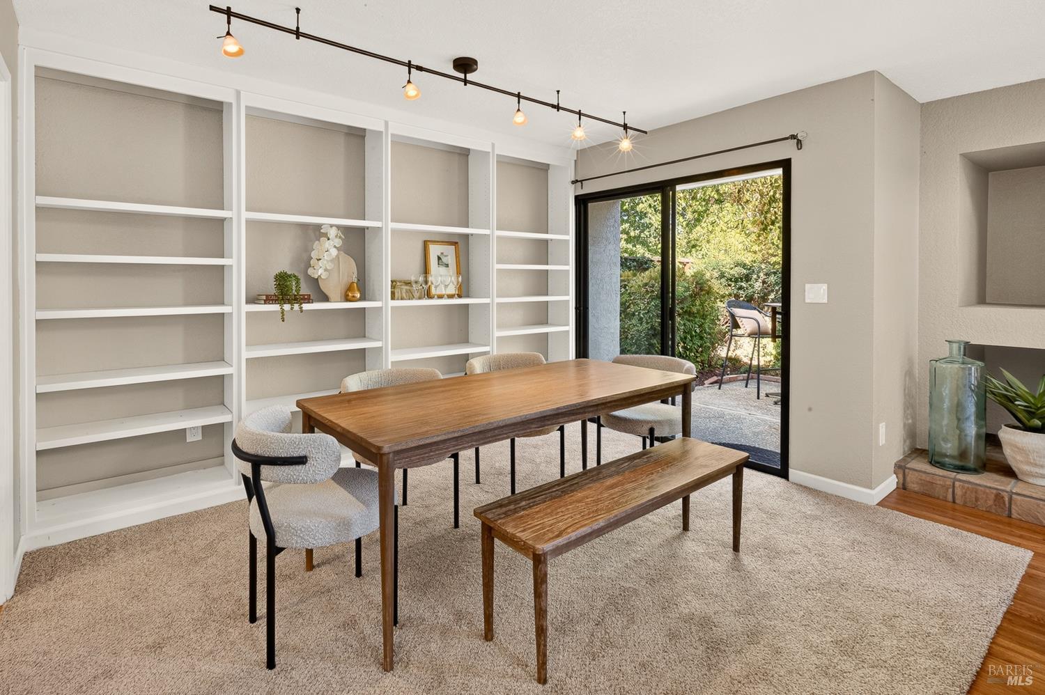 Dining room with built-in shelving, a wooden table and bench, and sliding glass doors to a leafy patio.