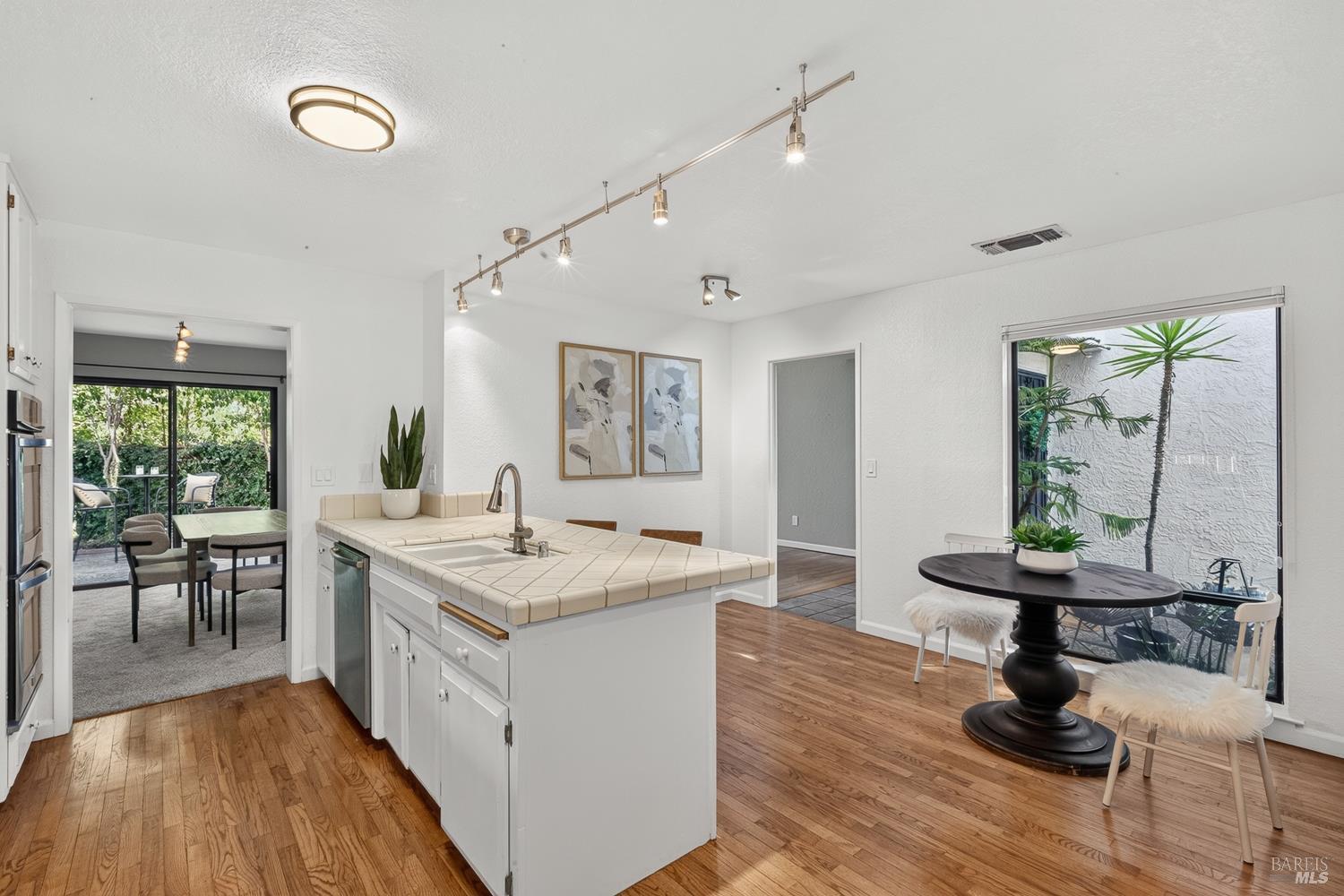 Kitchen and dining area with a tiled island, hardwood floors, and windows overlooking a leafy patio.