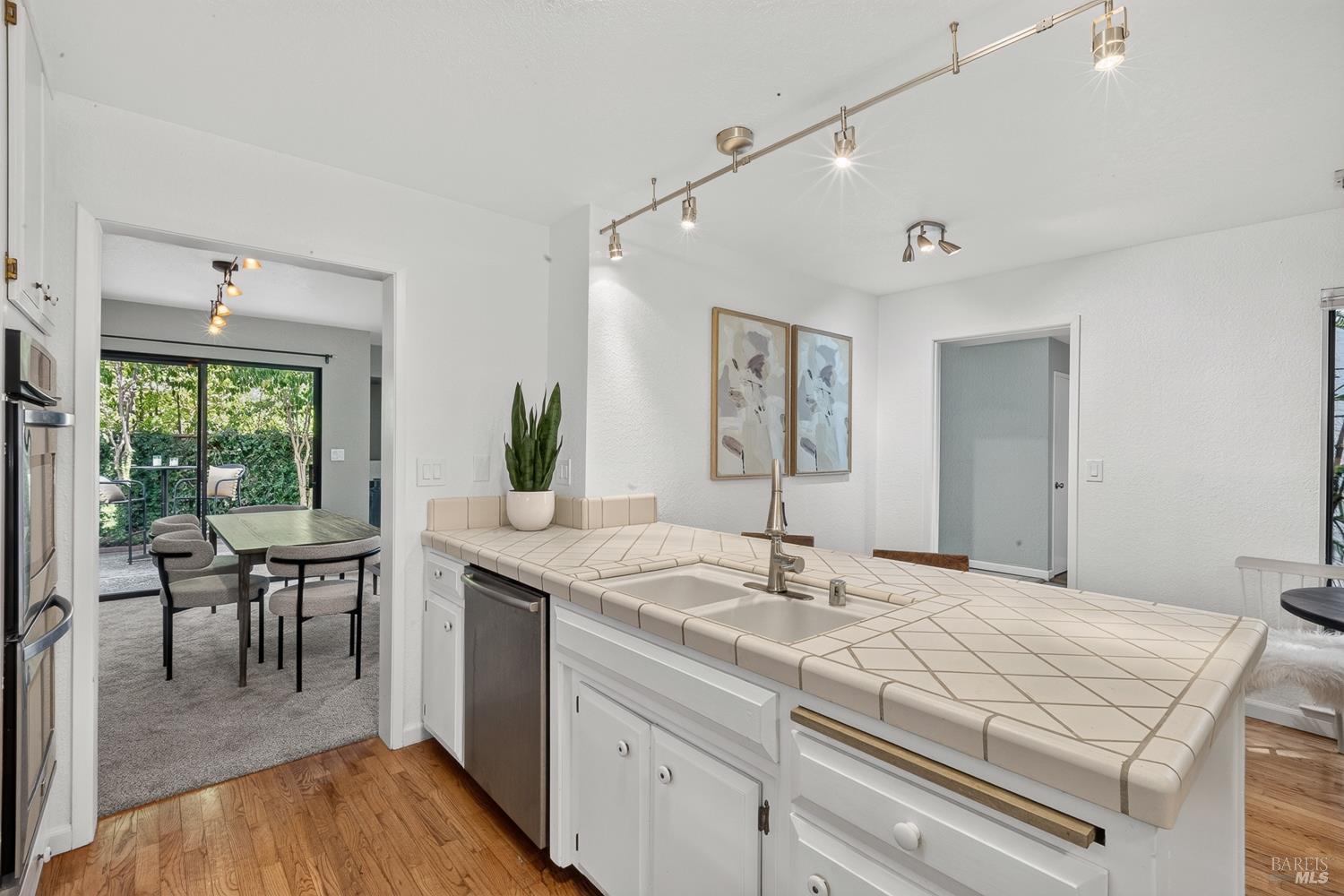 Kitchen with a large tiled peninsula and sink, opening to a dining area and leafy outdoor space.