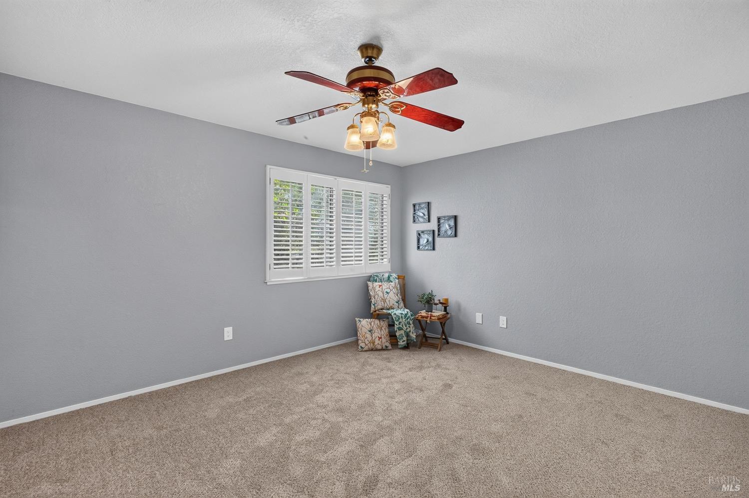 Bedroom with gray walls, beige carpet, plantation shutters, and a ceiling fan.