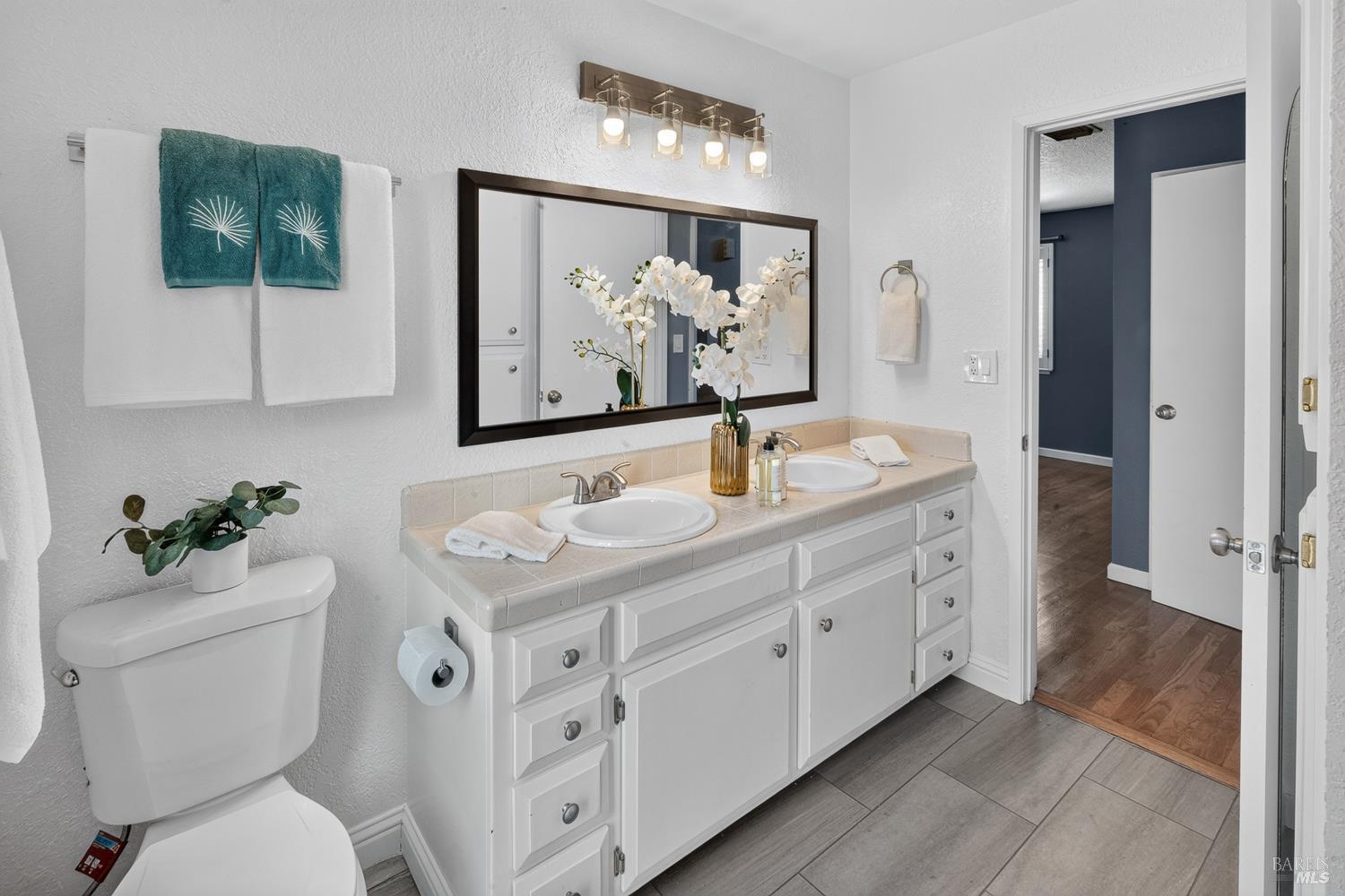 Bathroom with a white double-sink vanity, framed mirror, and gray tile flooring.