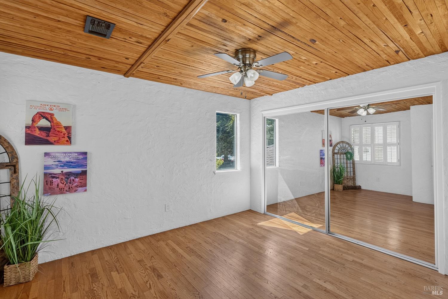 Empty bedroom with a wood-plank ceiling, hardwood floors, and mirrored sliding closet doors.