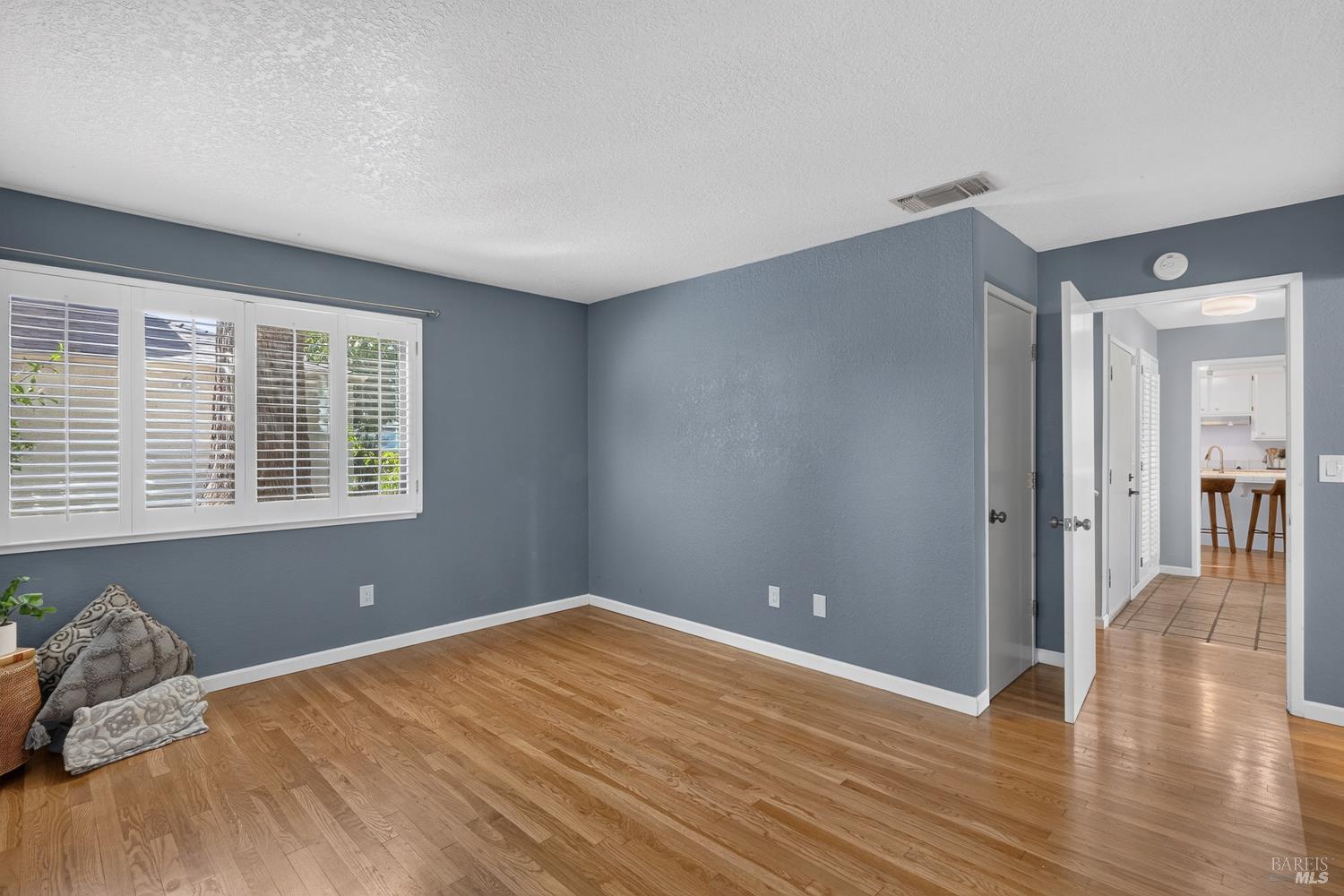 Room with hardwood floors, blue-gray walls, and a wide shuttered window.