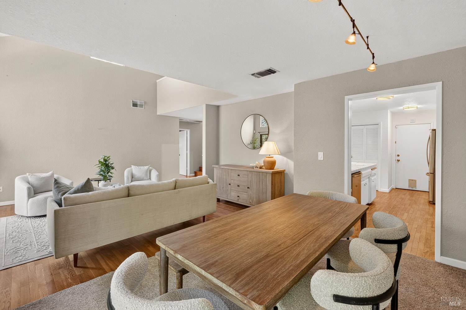 Open-plan living and dining area with a large wooden table, upholstered chairs, and neutral seating.