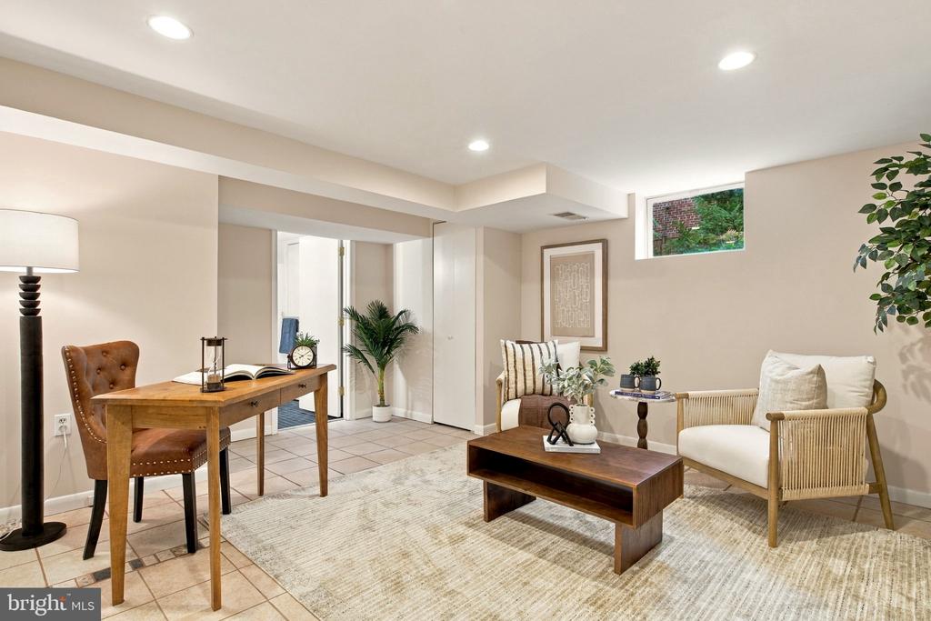 Staged living room with a wooden desk, brown leather chair, and white armchair.