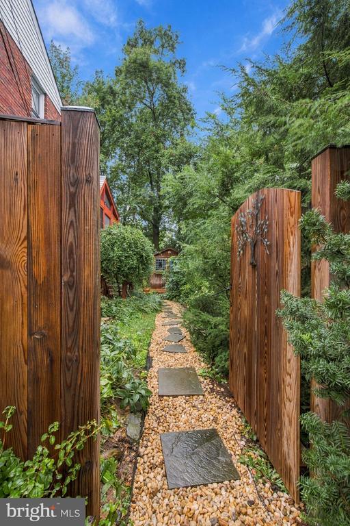 Garden path with stepping stones winding between wooden fences and lush greenery.
