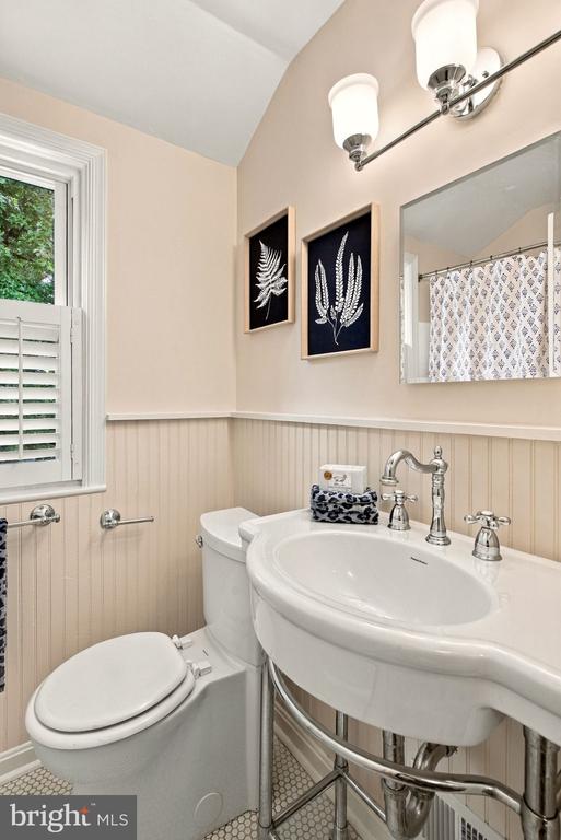 Bathroom with a white console sink, beadboard wainscoting, botanical prints, and a shuttered window.
