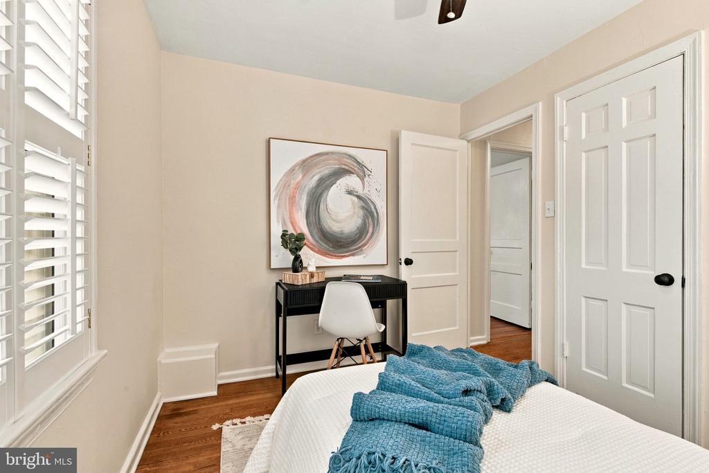 Bedroom with plantation shutters, hardwood floors, and a desk beneath circular artwork.