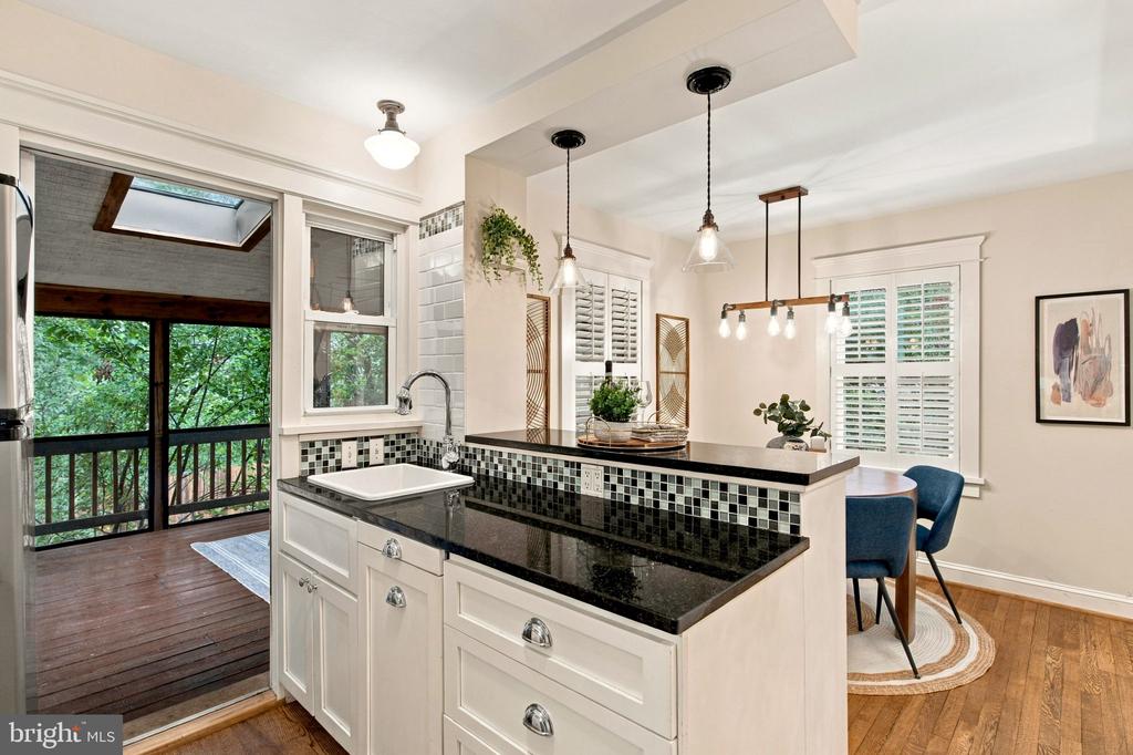 Kitchen with black countertops and breakfast bar beside a glass door opening onto a leafy deck.