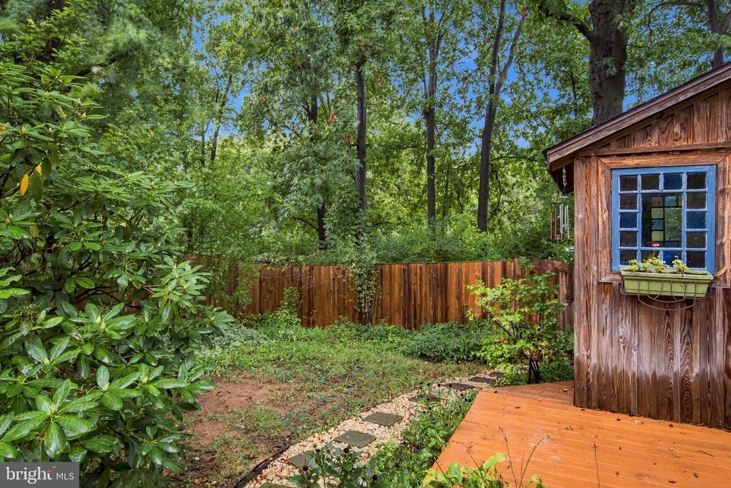 Wooded backyard with a wooden deck, stepping-stone path, and small wood-sided shed.