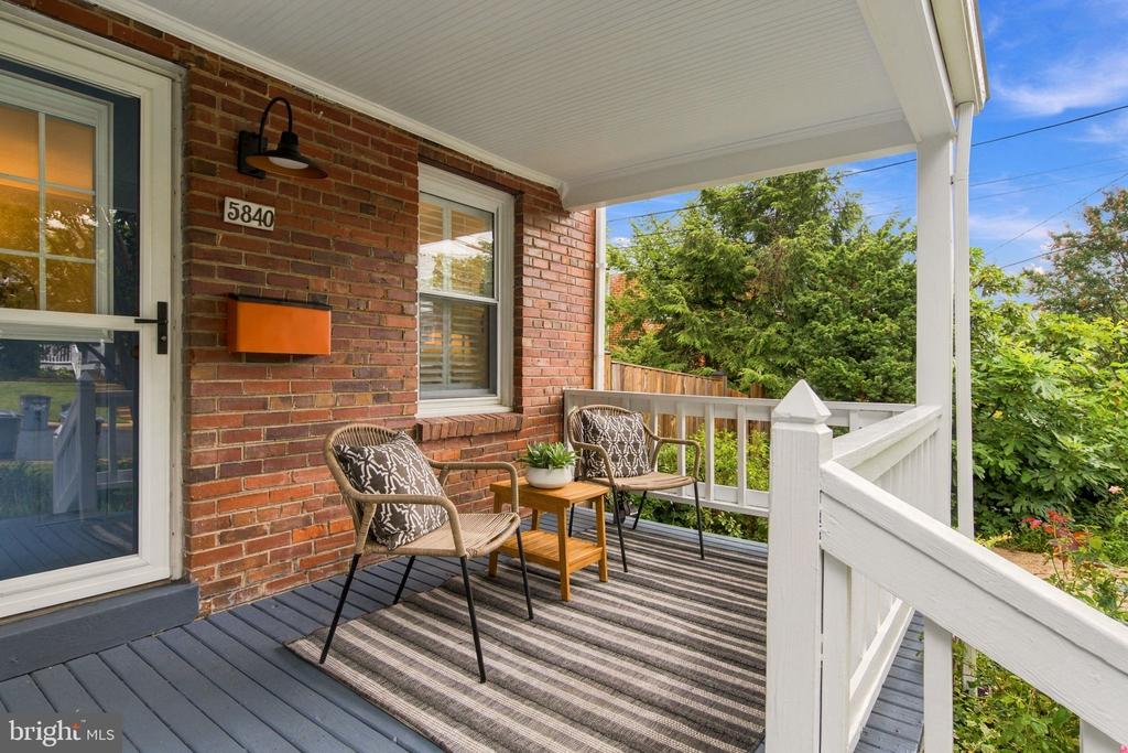Covered brick porch with two chairs, a small table, and a striped rug.