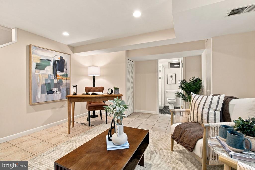 Staged living room with a desk, sofa, coffee table, and bathroom doorway.