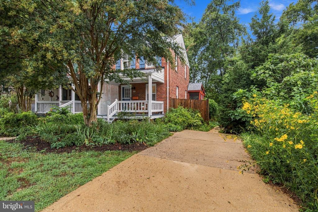 Red brick two-story home with a covered porch, broad driveway, and lush garden landscaping.