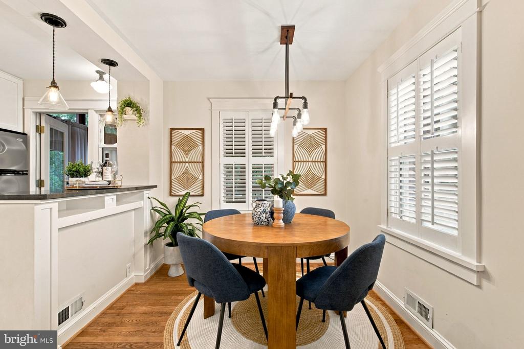 Dining room with a round wood table, blue chairs, plantation shutters, and hardwood floors.