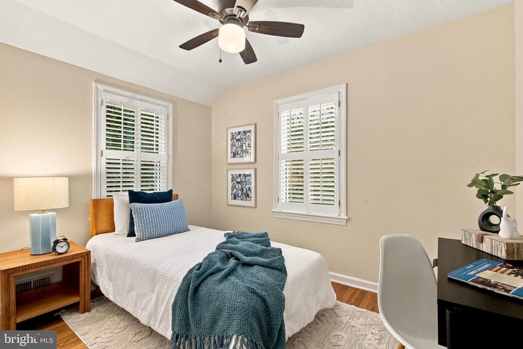 Staged bedroom with a white bed, blue throw, shuttered windows, and ceiling fan.