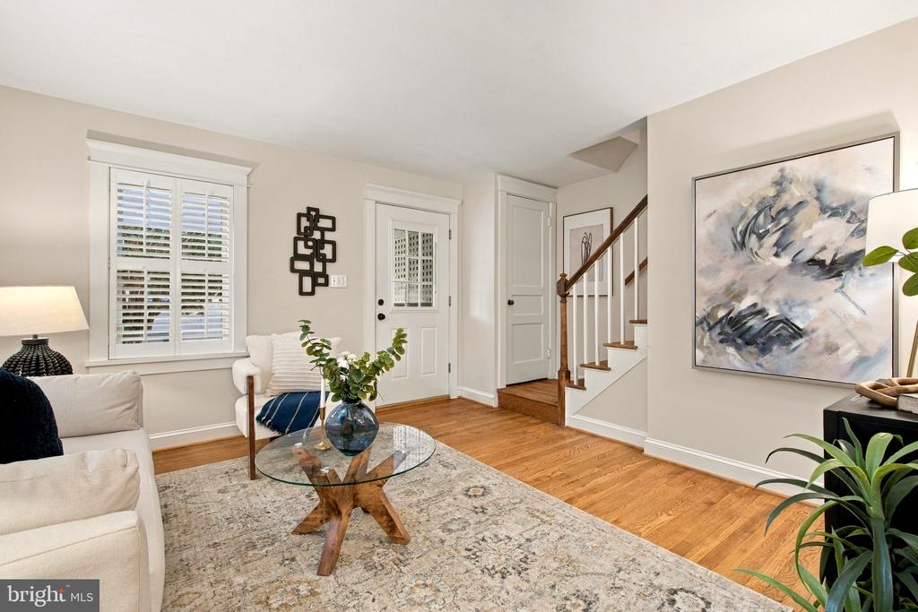 Living room with white sofas, a glass coffee table, shuttered windows, and a staircase.