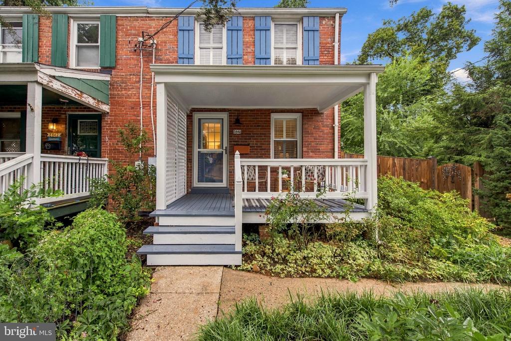 Red brick townhouse with colorful shutters, a covered porch, and landscaped front garden.