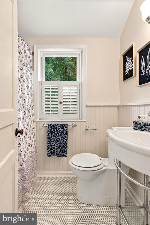 Bathroom with a shuttered window, beadboard wainscoting, patterned shower curtain, and curved sink.
