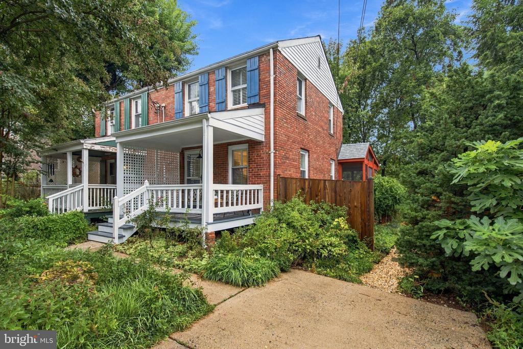 Two-story red brick house with blue shutters, a covered white porch, and a landscaped yard.