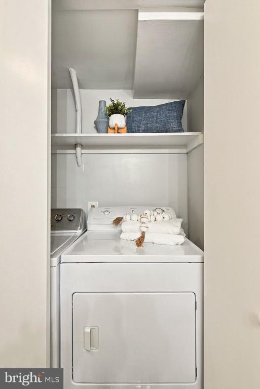 Laundry closet with white appliances, folded towels, and a shelf with decorative items.