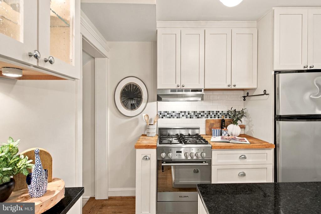 Kitchen with white cabinets, butcher-block counters, stainless steel appliances, and a black stone island.