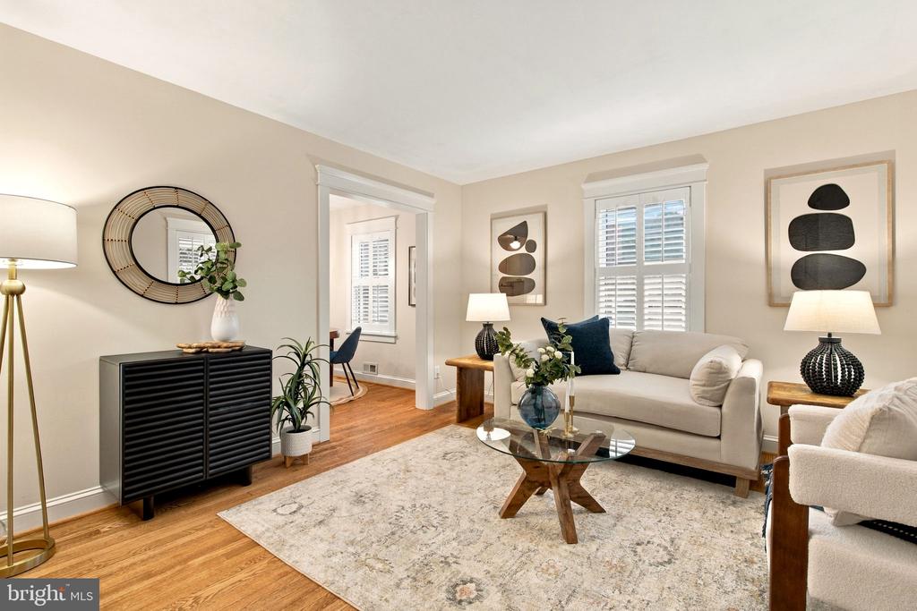 Staged living room with a cream sofa, glass coffee table, and plantation shutters.