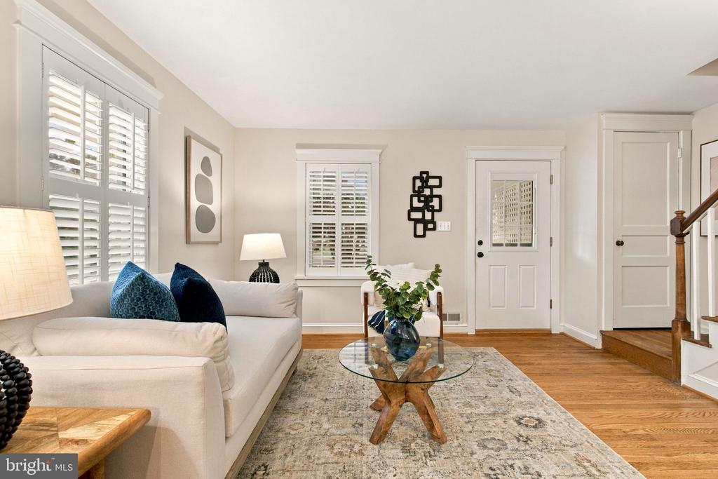 Furnished living room with a white sofa, plantation shutters, and a glass coffee table.