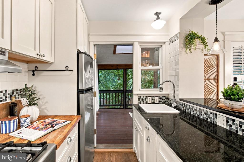 Kitchen with white cabinets and black counters opening onto a leafy deck.
